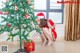 A woman in a santa claus outfit is putting a present under a Christmas tree.