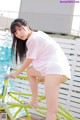 A young woman in a pink shirt and yellow shorts posing by a pool.