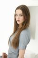 A woman with long brown hair standing in front of a white wall.