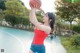 A woman in a red shirt and blue shorts holding a basketball.