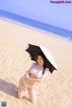 A woman in a white bikini holding an umbrella on the beach.