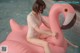 A woman sitting on an inflatable flamingo in a pool.