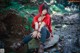 A woman in a red hooded outfit sitting on a rock in the woods.