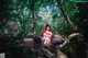 A woman in a red riding hoodie sitting on a rock in the woods.